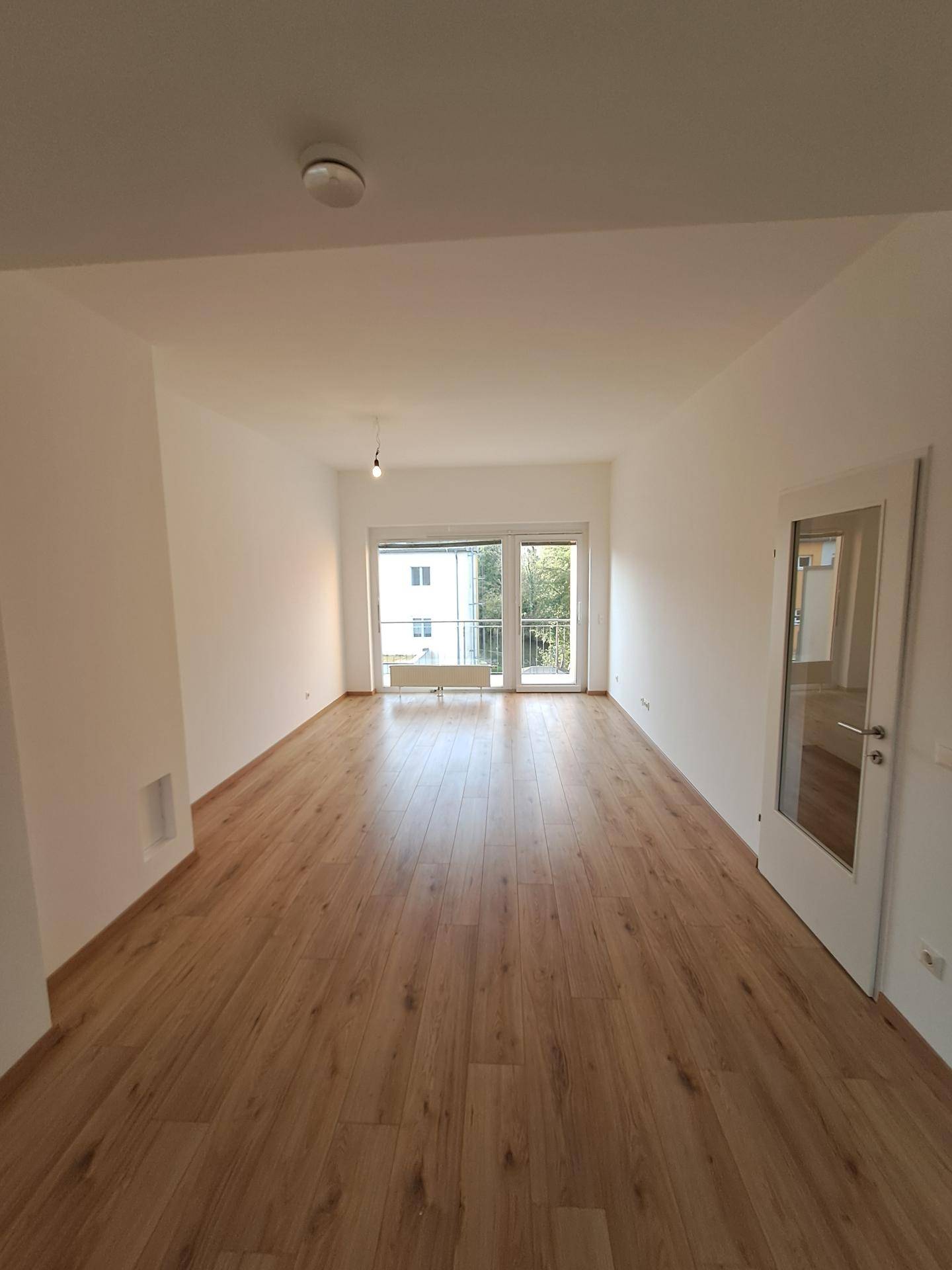 Langes Wohnzimmer mit Laminatboden und breiter Fensterfront, die den Raum hell und einladend macht.