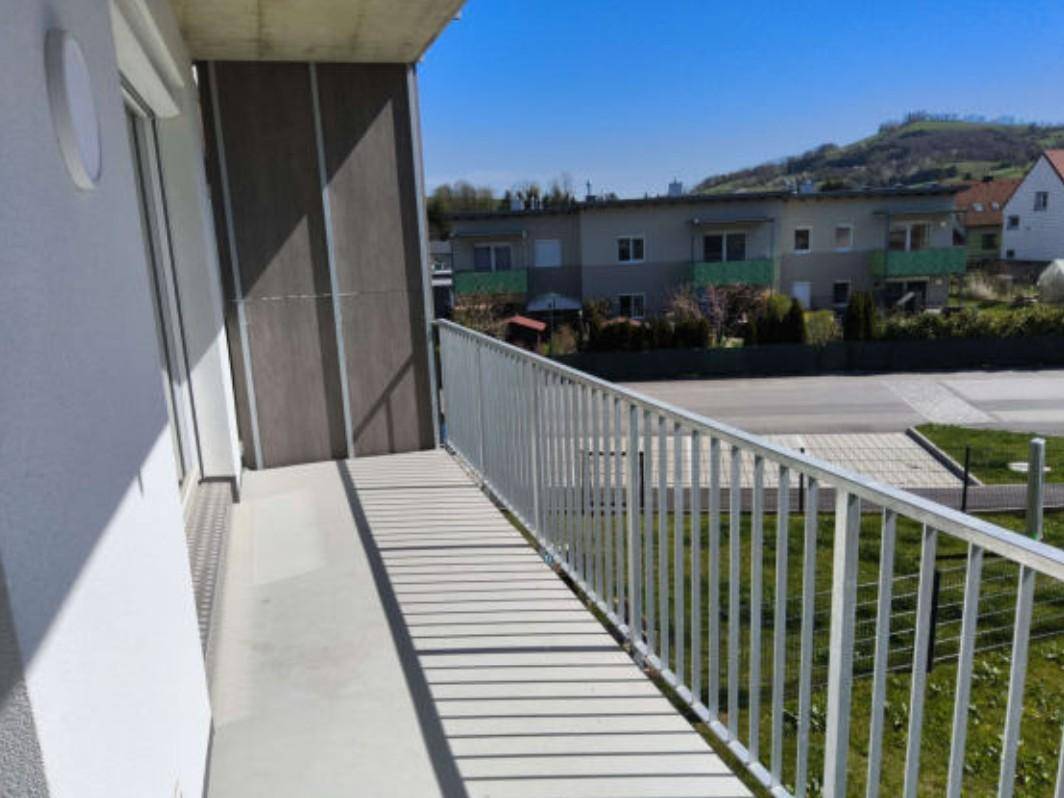Sonniger Balkon mit Blick auf die umliegende Landschaft und weitere Wohngebäude unter blauem Himmel.