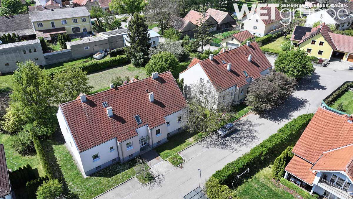 Luftaufnahme von Wohnhäusern mit roten Dächern, umgeben von Gärten und einer ländlichen Landschaft.
