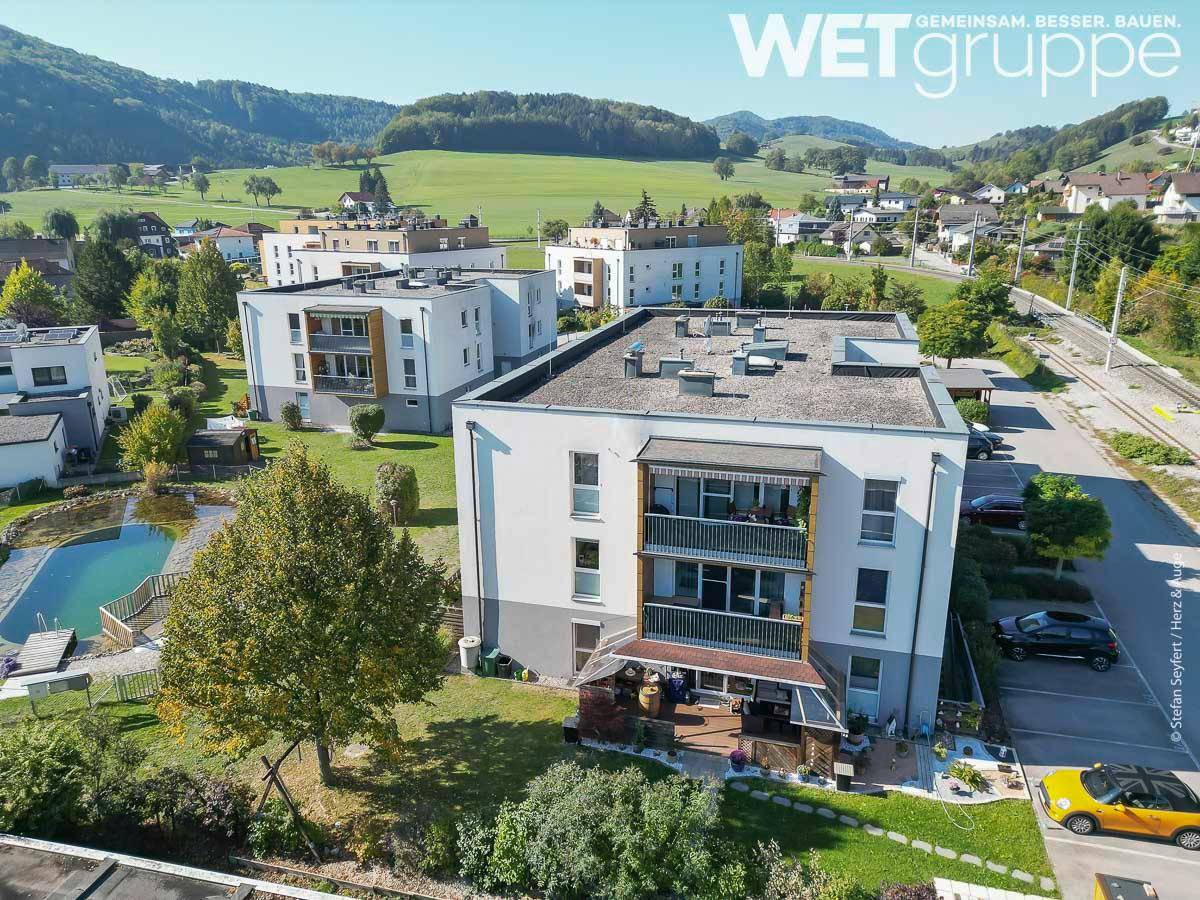 Übersicht der Wohnanlage mit modernen Gebäuden, Grünflächen und einem Teich.