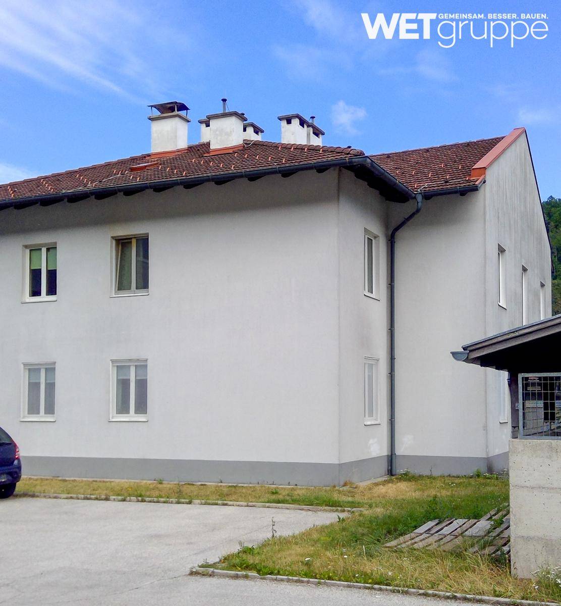 Rückansicht eines modernen Wohngebäudes mit weißer Fassade, Satteldach und Außenparkplätzen.