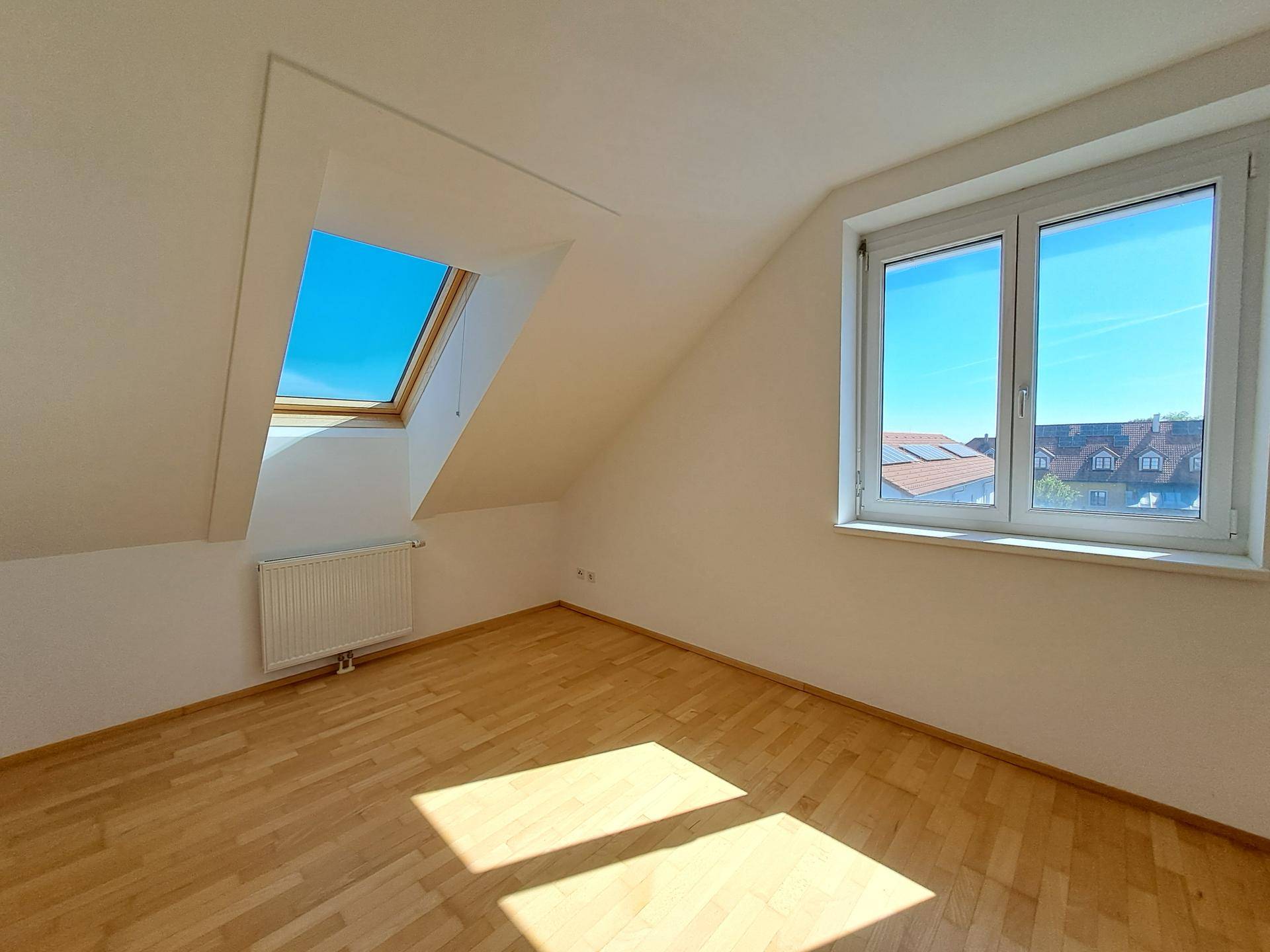 Helles Zimmer im Dachgeschoss mit Holzfußboden, großem Fenster und Dachfenster.