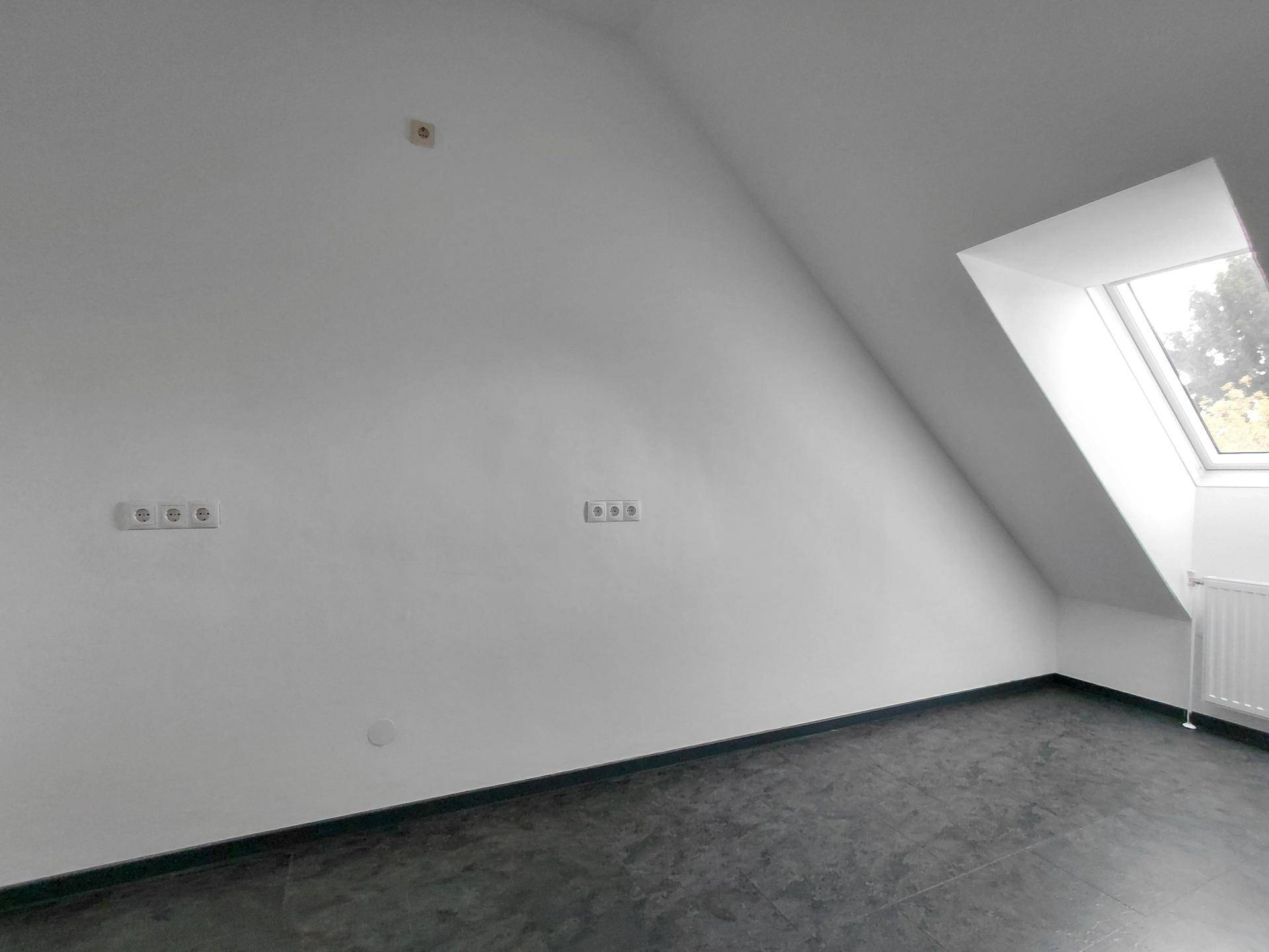 Dachgeschosszimmer mit dunklem Fliesenboden, schräger Decke und einem Dachfenster für natürliches Licht.