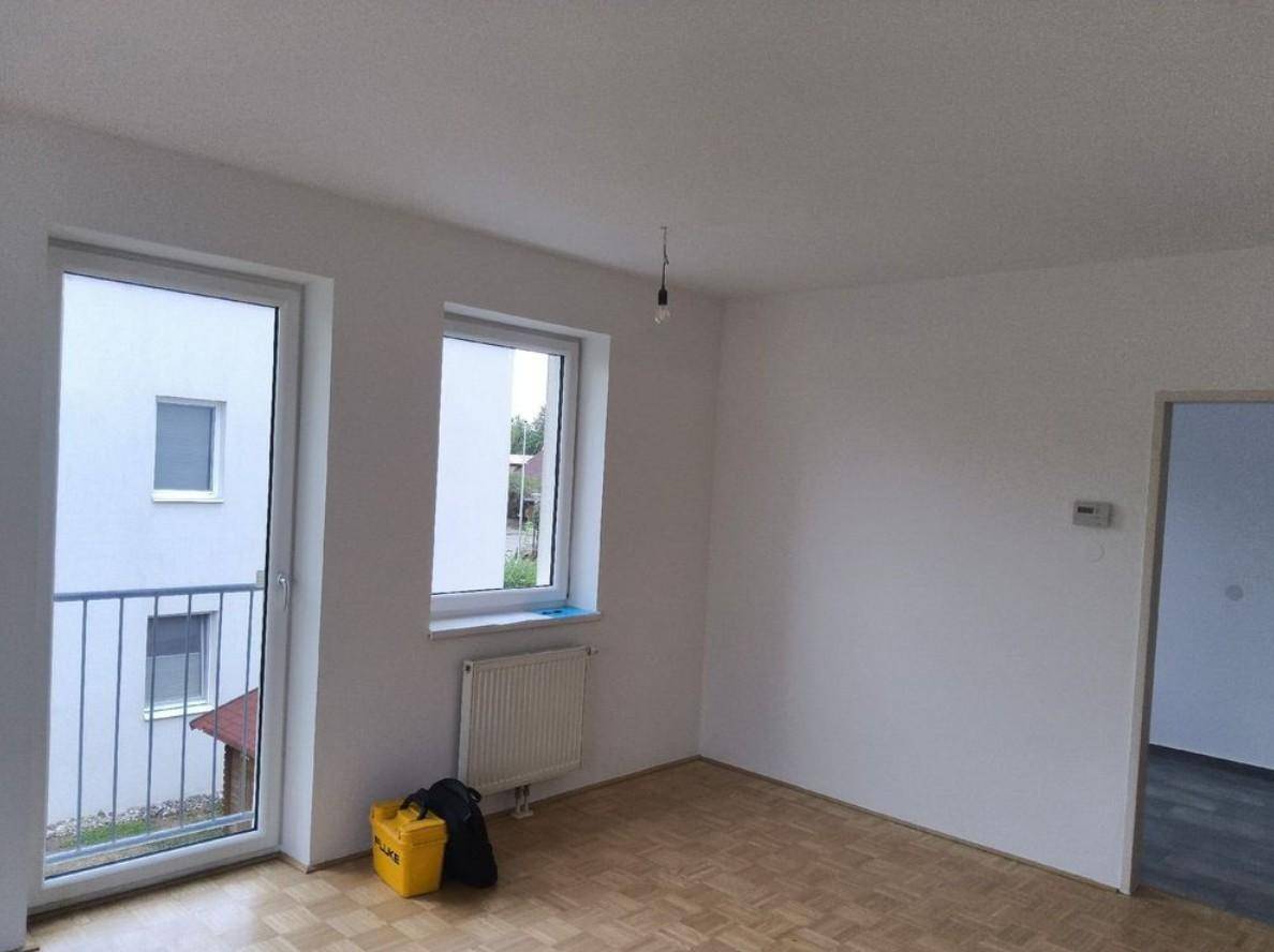 Heller Wohnraum mit Parkettboden, Heizkörper und Balkonzugang mit Blick auf die Nachbarschaft.