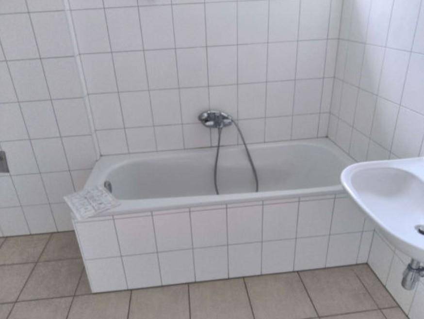 Badezimmer mit weißen Fliesen, einer Badewanne und einem einzelnen Waschbecken.