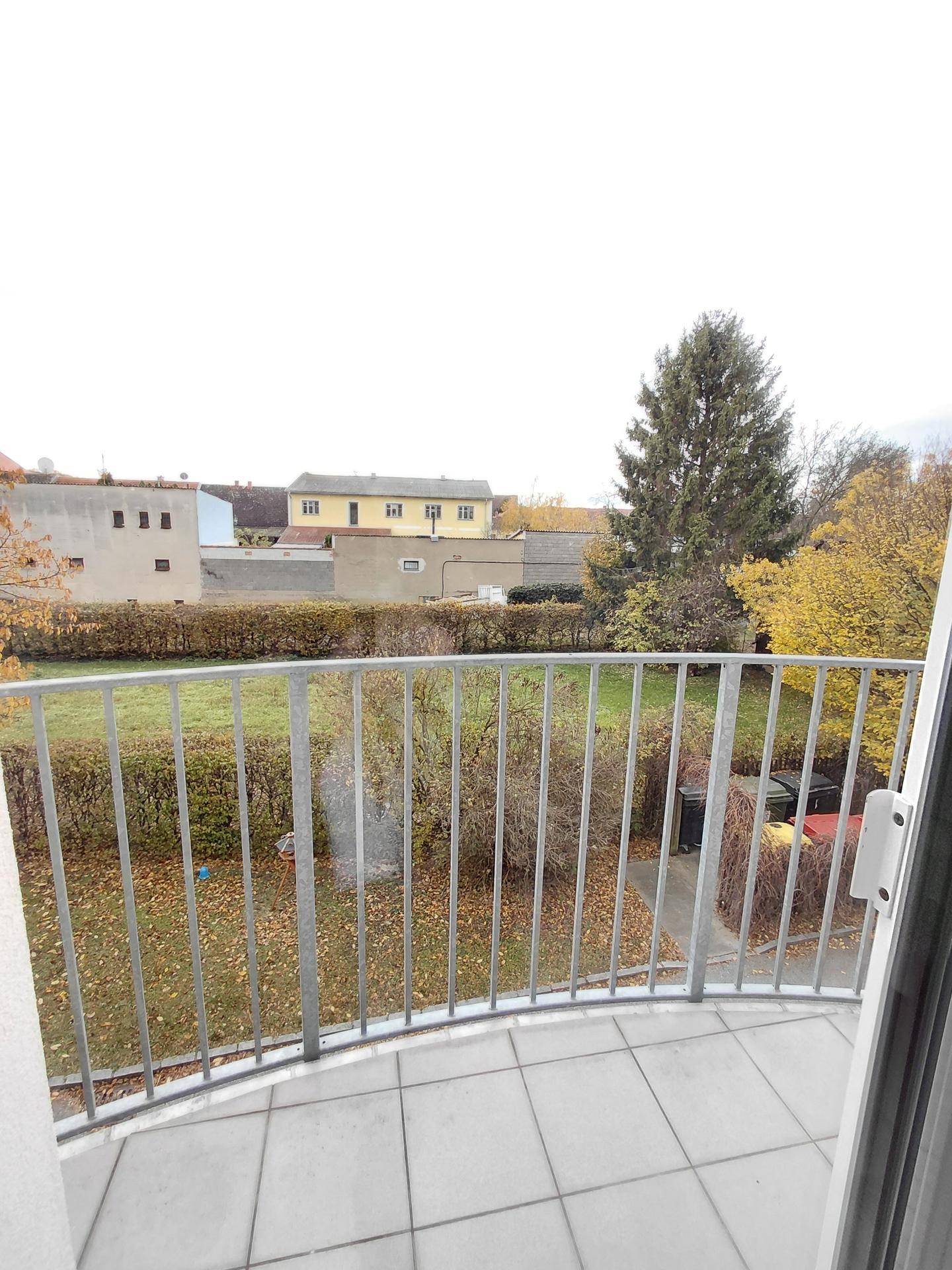 Balkon mit Fliesenboden und Metallgeländer, bietet Blick auf grüne Umgebung und Bäume.