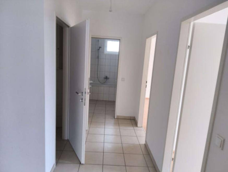 Flur mit Fliesenboden und Zugang zu einem Badezimmer, das eine Badewanne und weiße Fliesen zeigt.