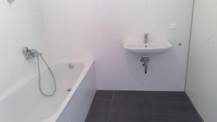 Modernes Badezimmer mit Badewanne, Einzelwaschbecken und dunklen Bodenfliesen.