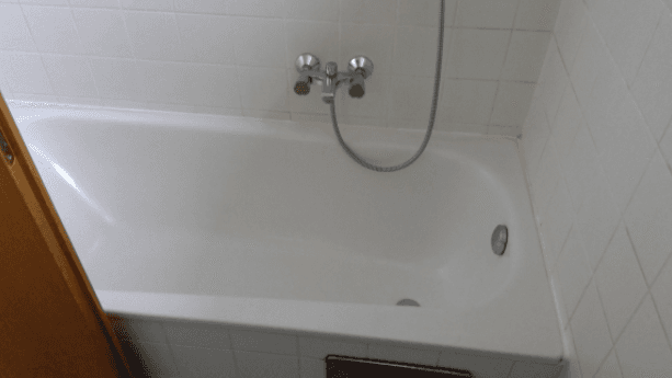 Weiße Badewanne mit Duscharmatur und weißen Fliesen an den Wänden, in einem Badezimmer.
