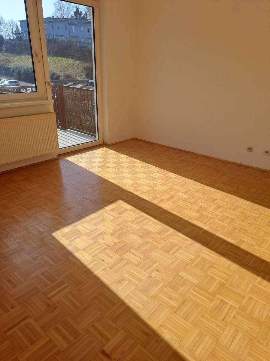 Helles Zimmer mit Parkettboden und Zugang zu einem Balkon mit Aussicht.