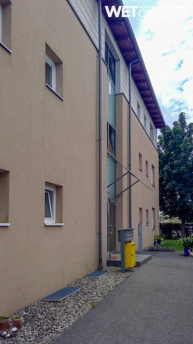 Seitenansicht eines Mehrfamilienhauses mit beiger Fassade und mehreren Fenstern.