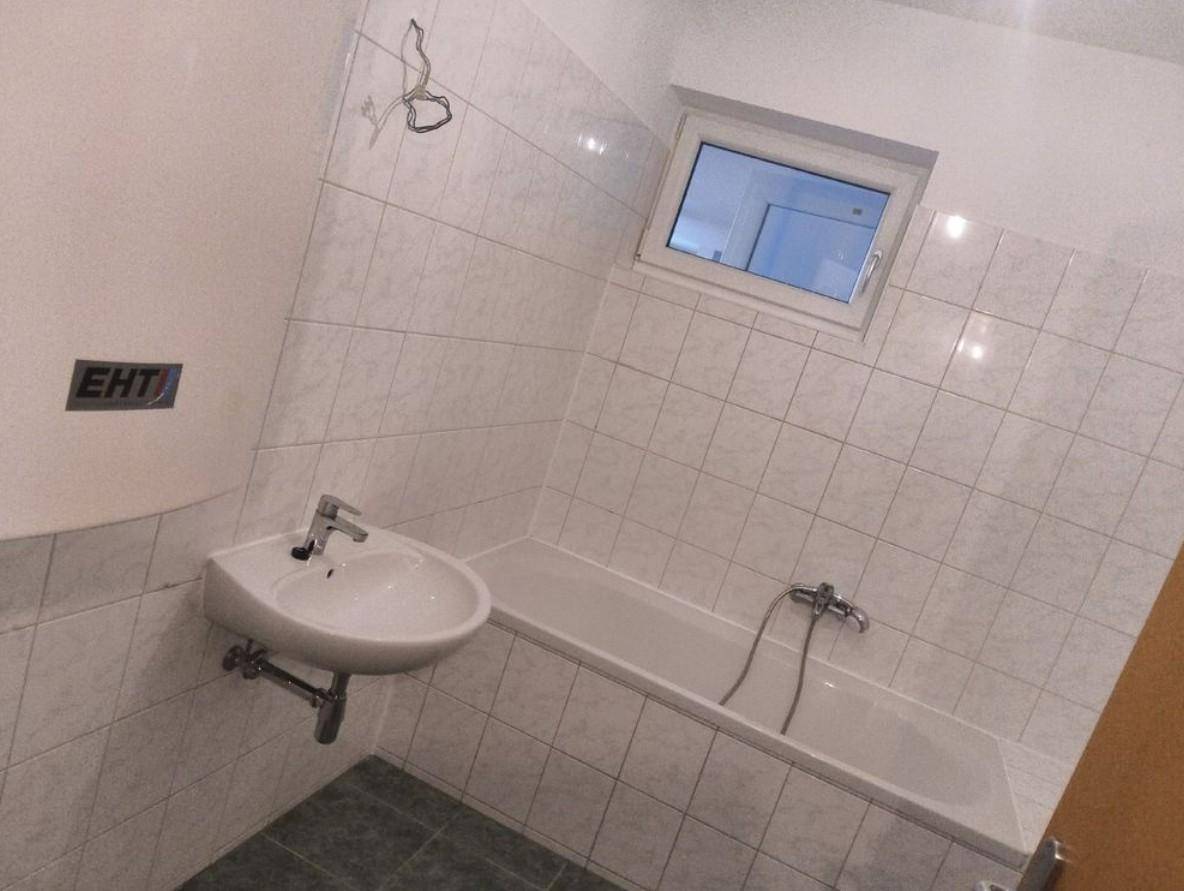 Helles Badezimmer mit weißen Fliesen, Badewanne, Waschbecken und Fenster für natürliche Belüftung.