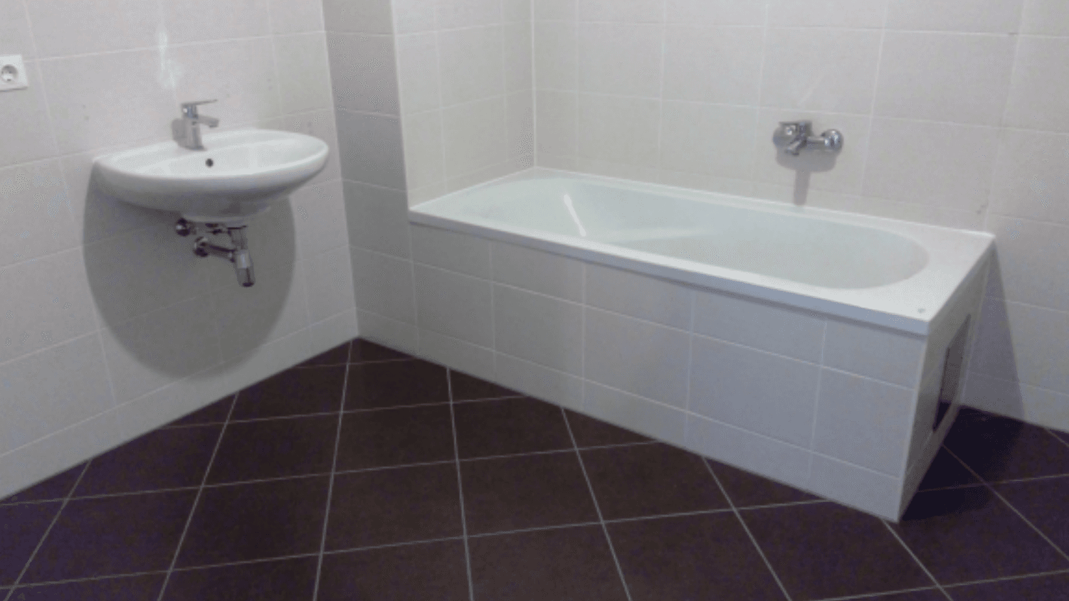 Helles Badezimmer mit Badewanne, Waschbecken und hellen Fliesen an Wänden und Boden.