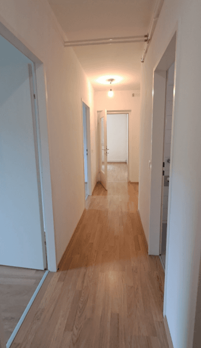 Langer, heller Flur mit Laminatboden, weißen Wänden und mehreren Türen zu angrenzenden Räumen.