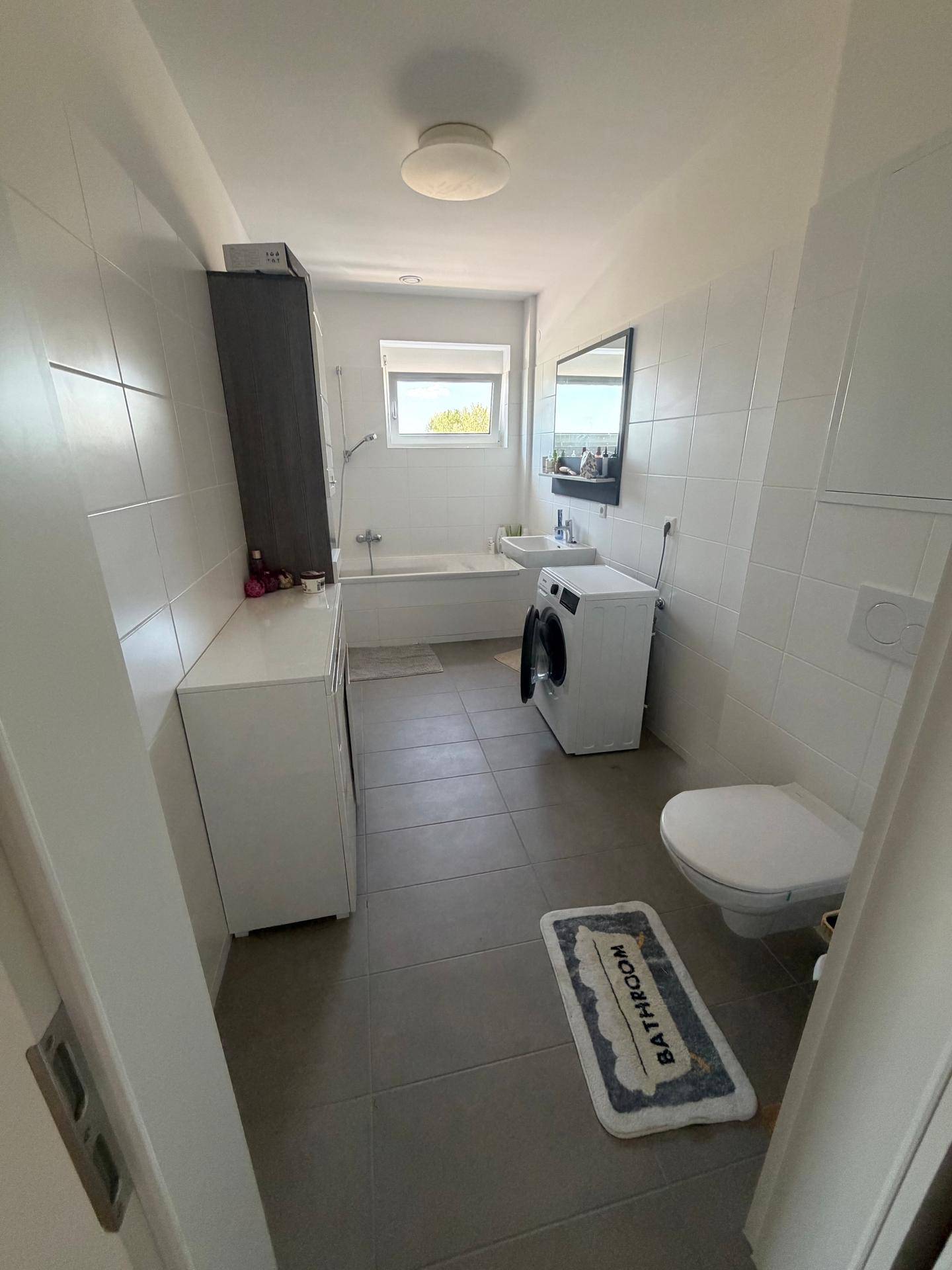 Modernes Badezimmer mit Badewanne, WC, Waschmaschine und Fenster für Tageslicht.