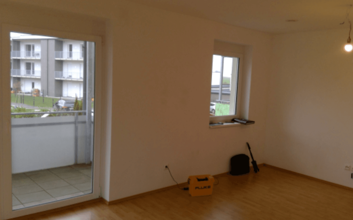 Leerer Raum mit Zugang zu einem Balkon, weißen Wänden und hellem Laminatboden, bietet viel Tageslicht.