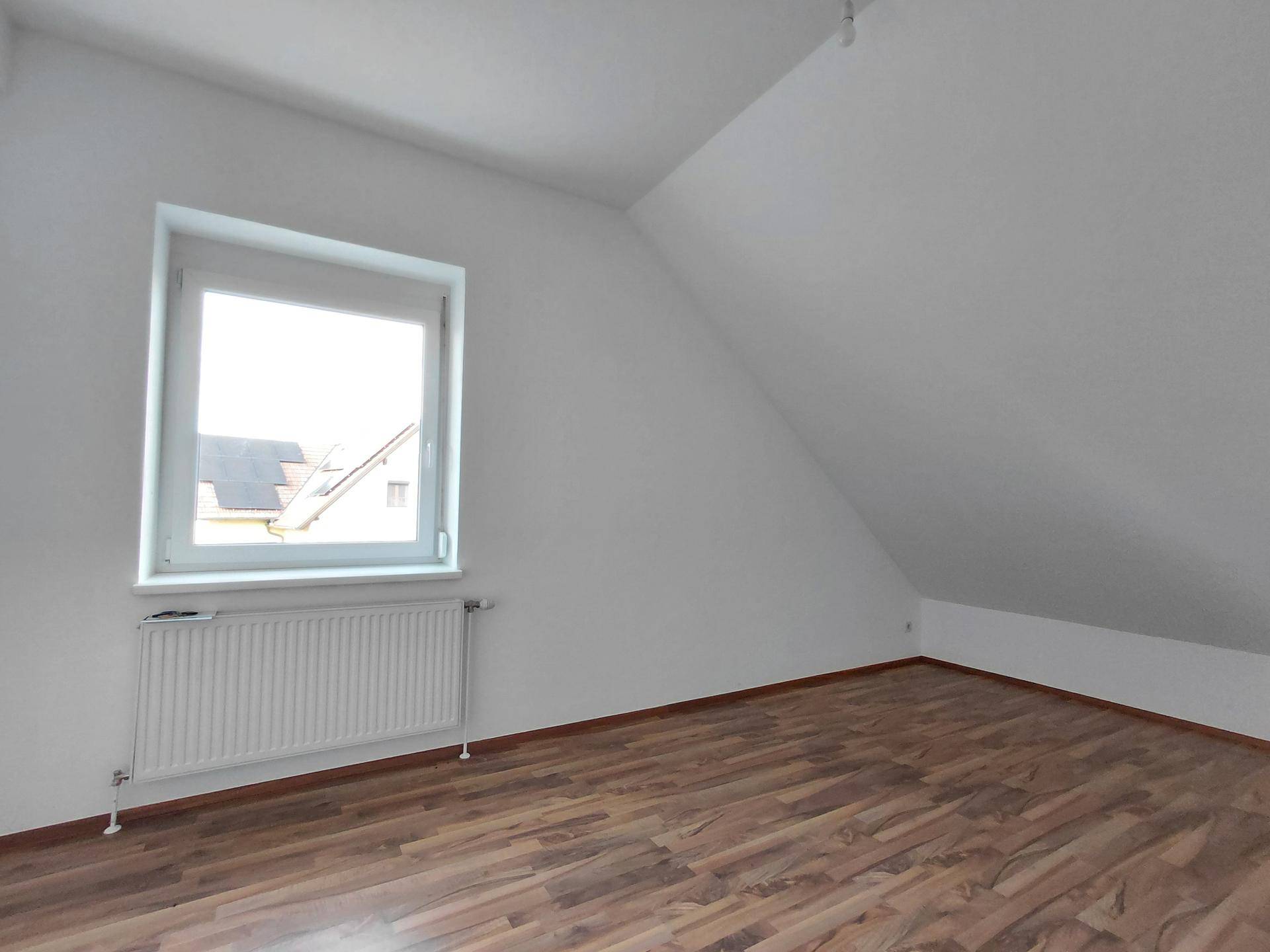 Helles Schlafzimmer im Dachgeschoss mit Schrägdecke, Fenster und Laminatboden.
