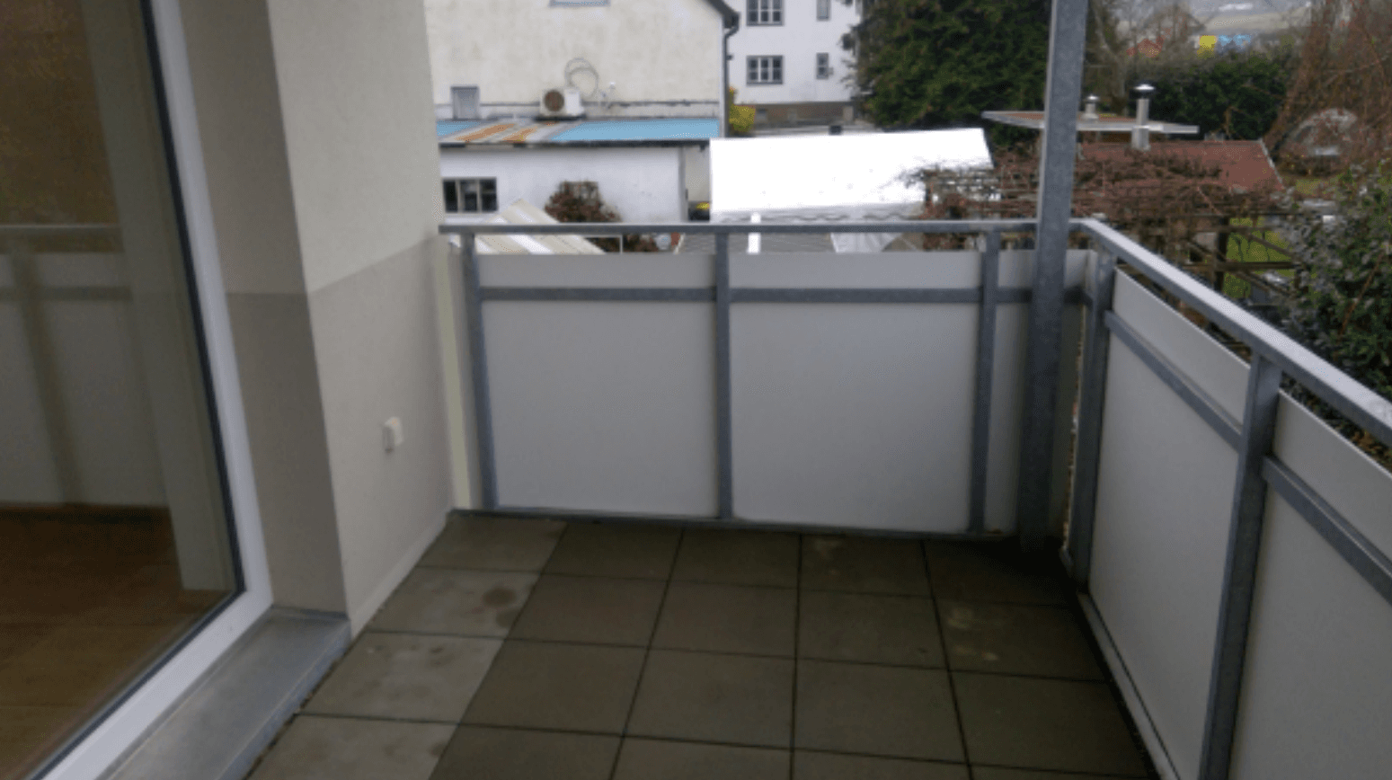 Kleiner Balkon mit Fliesenboden und Metallgeländer, bietet einen Blick auf die Nachbarschaft.