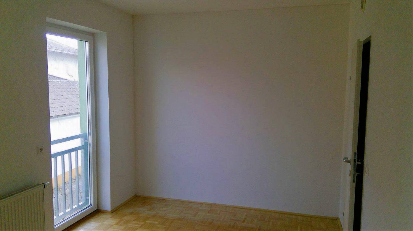Leerer Raum mit Holzboden und einem französischen Balkon, der für frische Luft sorgt.