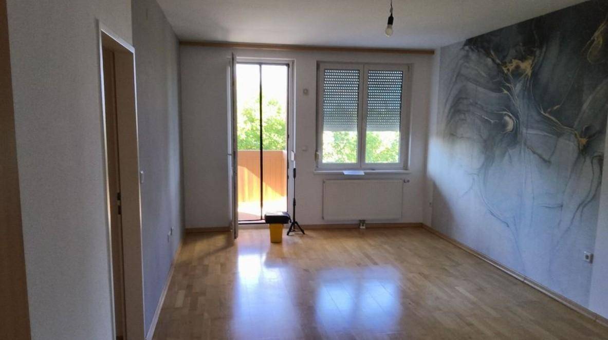 Helles Zimmer mit Holzboden, Zugang zum Balkon und einer modernen Akzentwand.