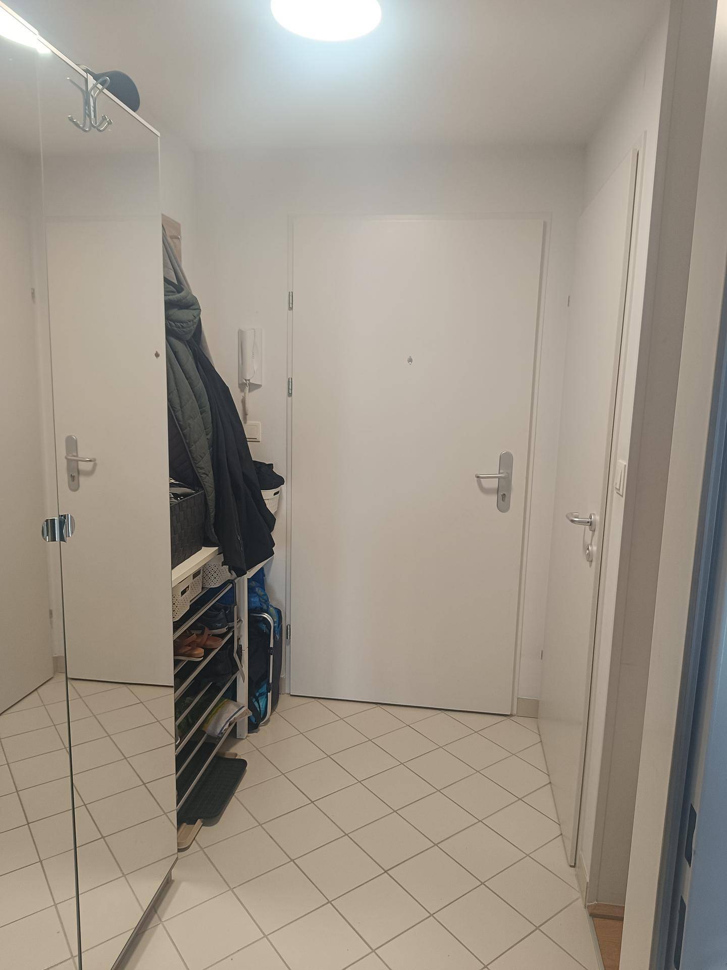 Heller Eingangsbereich mit weißen Fliesen, großem Spiegel und praktischem Stauraum für Schuhe.