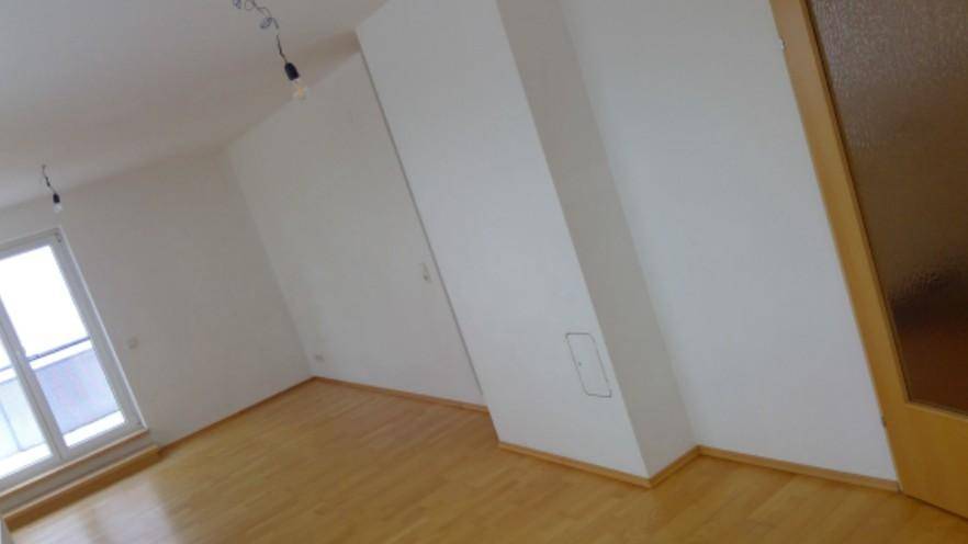 Geräumiger, heller Raum mit Holzfußboden, weißen Wänden und einer Dachschräge.