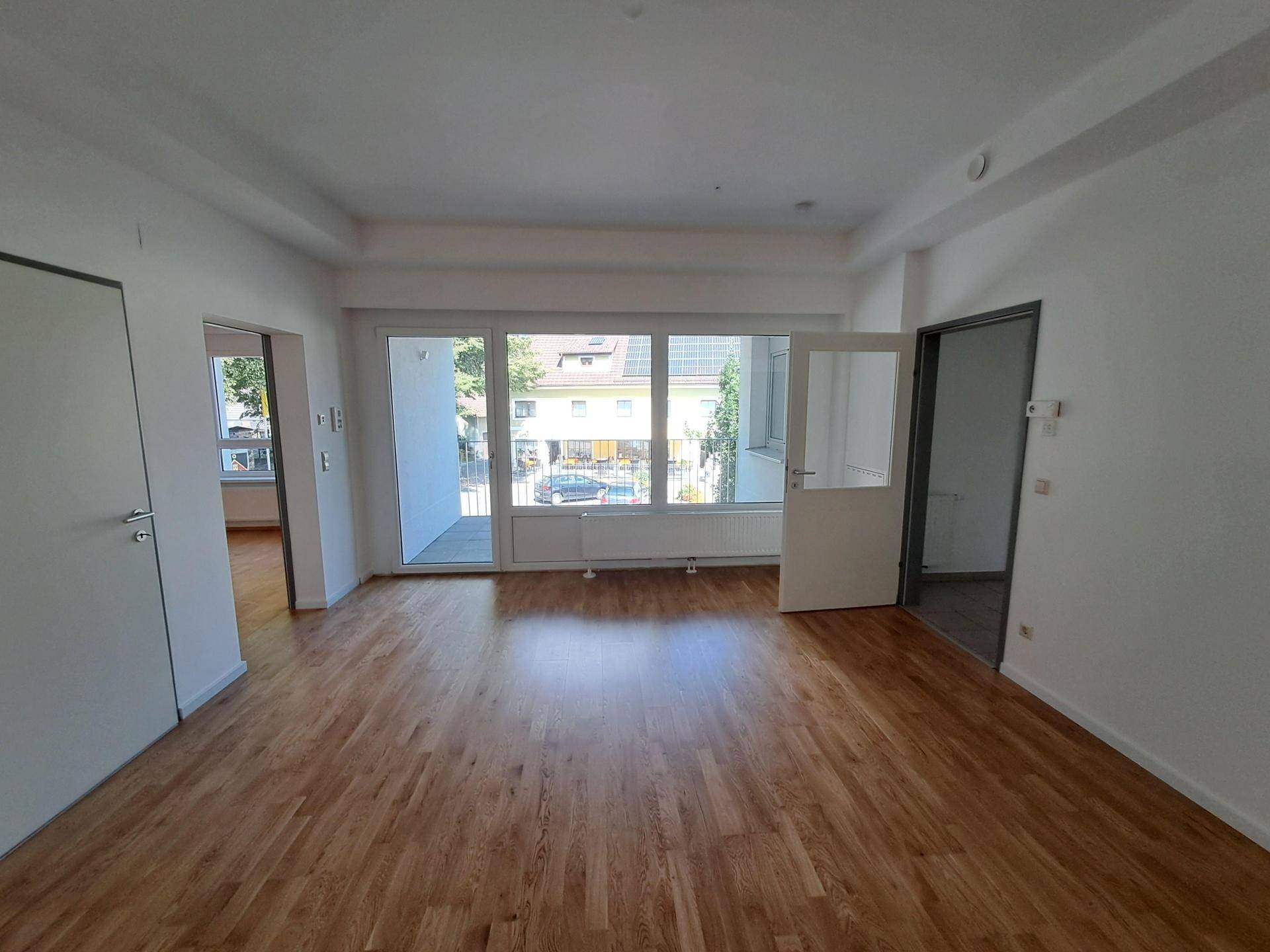 Geräumiges Wohnzimmer mit Holzparkettboden und Zugang zu einem Balkon oder einer Terrasse.