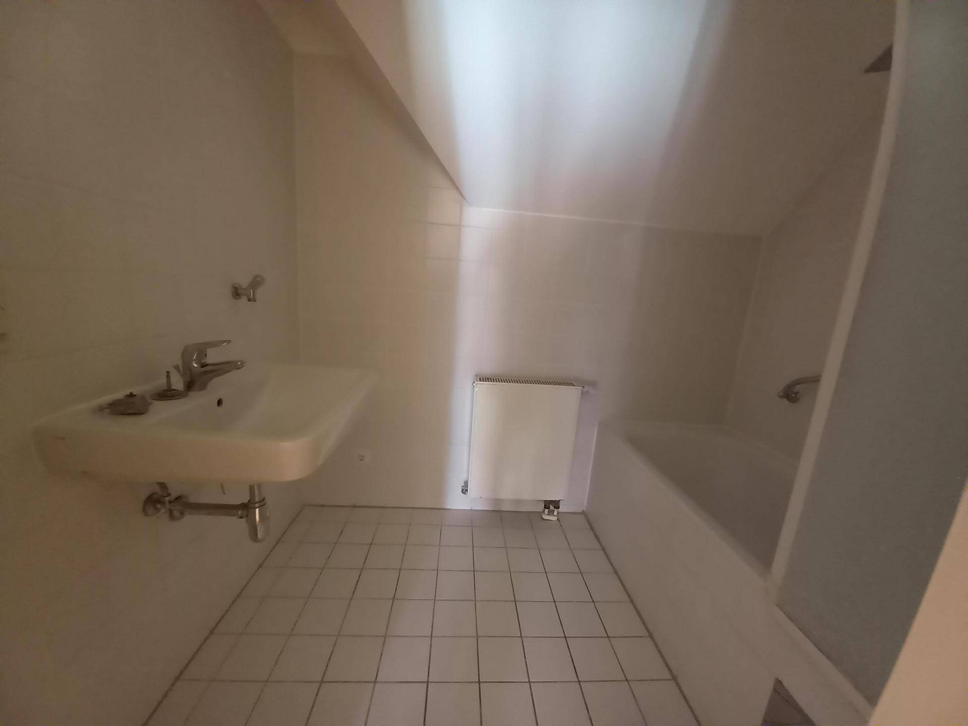 Badezimmer im Dachgeschoss mit weißen Fliesen, Waschbecken und Badewanne unter der Dachschräge.