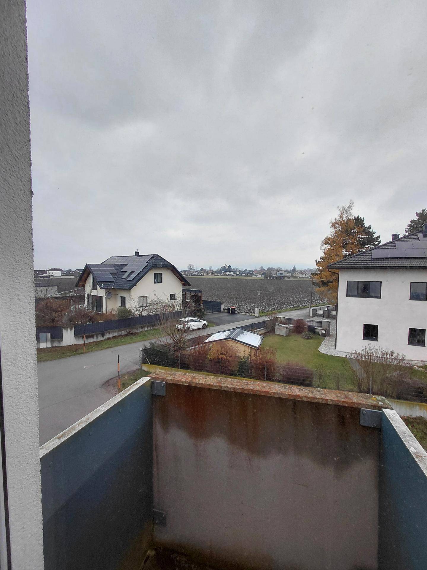 Blick vom Balkon auf die umliegende Wohngegend und weite Felder unter bewölktem Himmel.