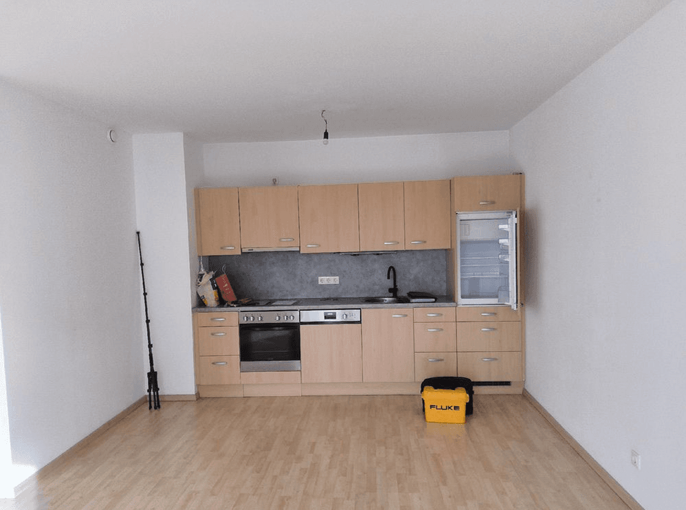 Helle Küche mit Holzschränken, integrierten Geräten und Parkettboden in einem offenen Raum.