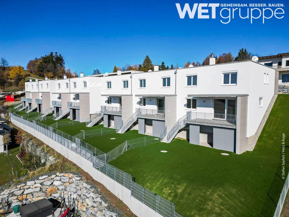 Reihenhäuser in moderner Architektur mit weißer Fassade und grünen Gärten in Hanglage.