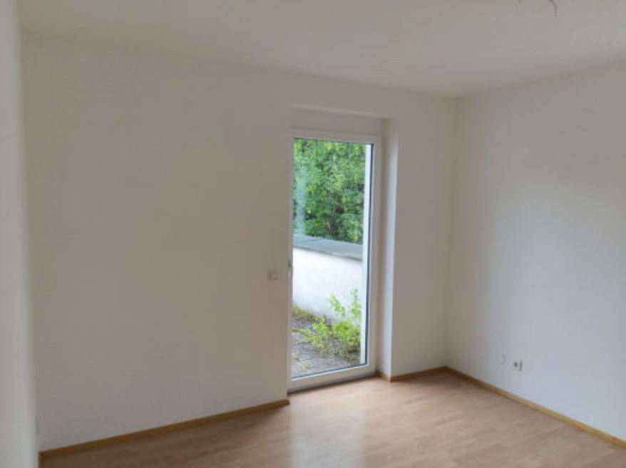 Helles Zimmer mit Holzboden und Zugang zu einem Außenbereich mit viel Grün.