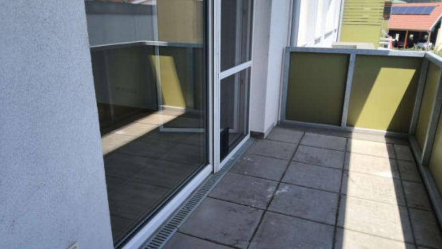 Balkon mit grauen Fliesen und moderner grün-grauer Brüstung, bietet Zugang zum Innenbereich.