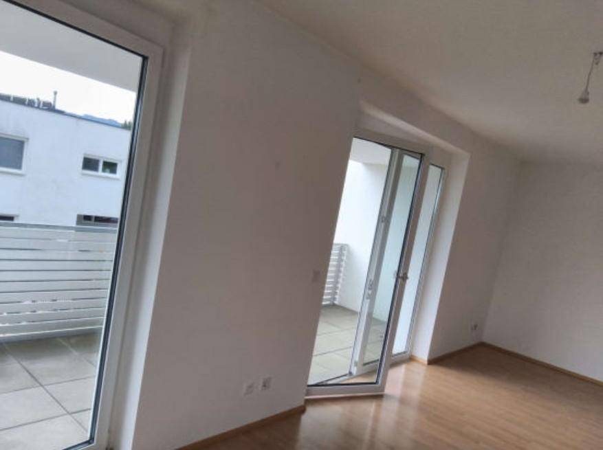 Heller Innenraum mit Holzboden und Zugang zu einem gefliesten Balkon, der viel Tageslicht hereinlässt.