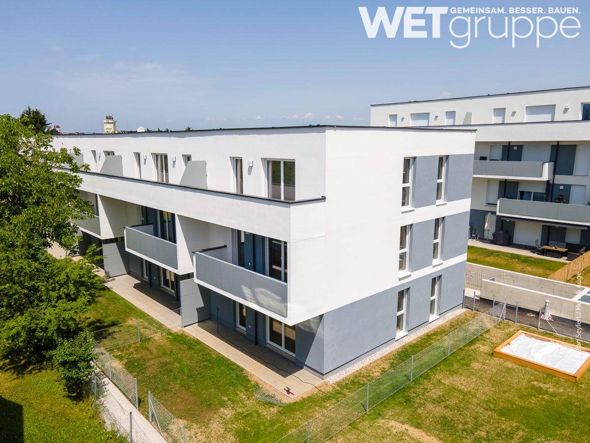 Neubau-Wohngebäude mit moderner Architektur, Balkonen und gepflegten Außenanlagen unter blauem Himmel.