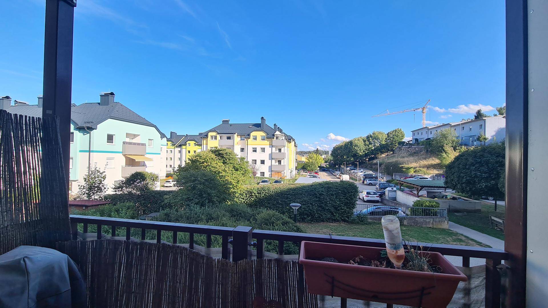 Blick vom Balkon auf die umliegenden Wohngebäude, Bäume und eine Straße.
