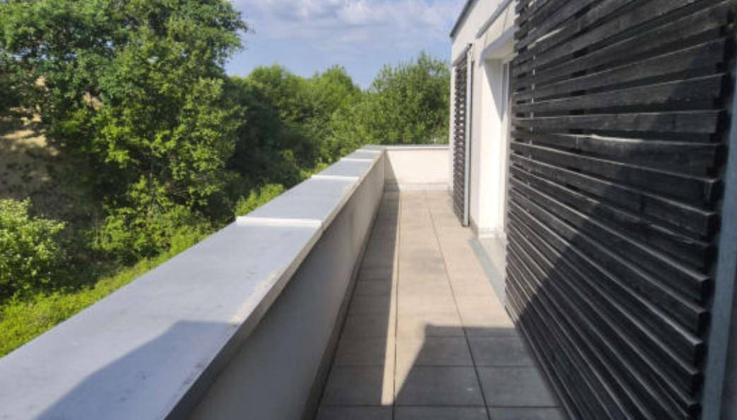Langer, schmaler Balkon mit Fliesenboden und Blick auf üppiges Grün und Bäume.
