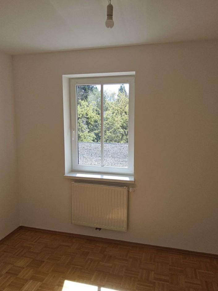 Helles Zimmer mit Parkettboden, weiß gestrichenen Wänden und Blick ins Grüne.