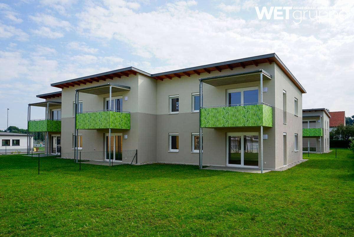 Modernes Mehrfamilienhaus mit grünen Balkonen und gepflegter Rasenfläche in einer ruhigen Umgebung.