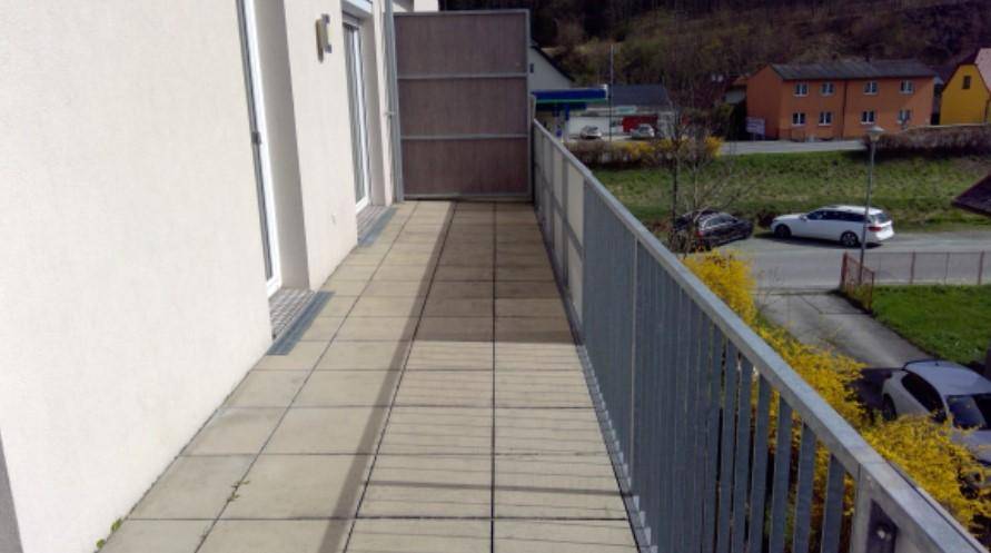 Langer, gefliester Balkon mit Metallgeländer und Blick auf die Umgebung und Hügel.