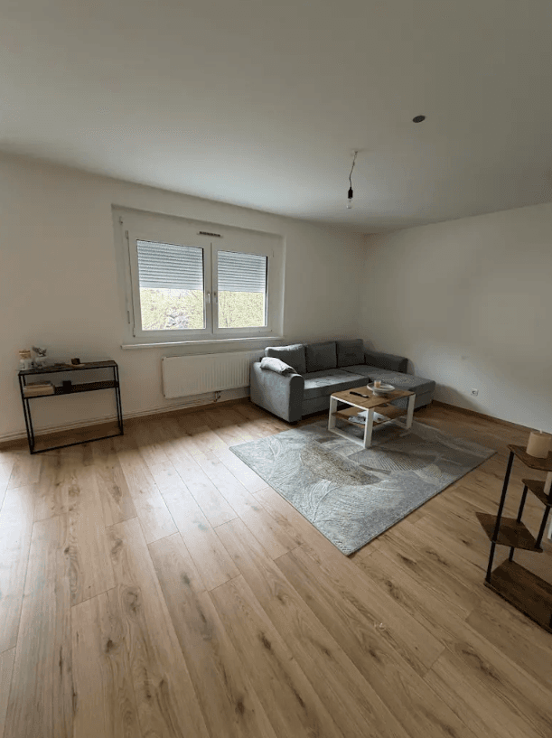 Helles Wohnzimmer mit großem Fenster, Sofa und modernem Teppich, einladend gestaltet.