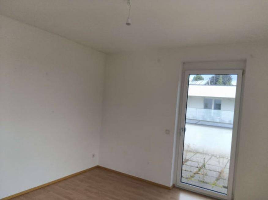 Leerer Raum mit Holzboden und einer Tür, die zu einem kleinen Außenbereich führt, ideal für individuelle Gestaltung.