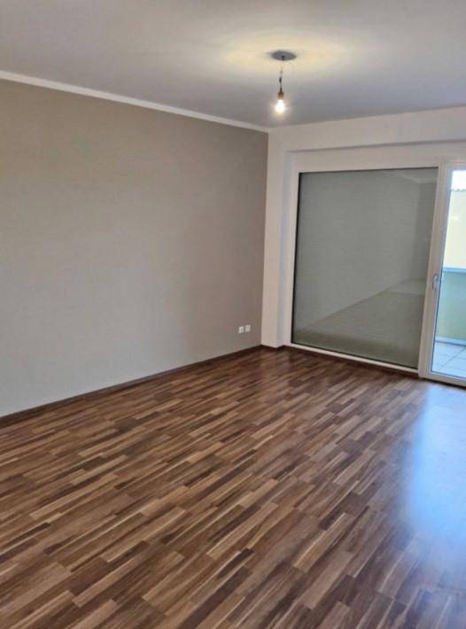 Geräumiges Zimmer mit Laminatboden, hellbeigen Wänden und Zugang zu einem Außenbereich.