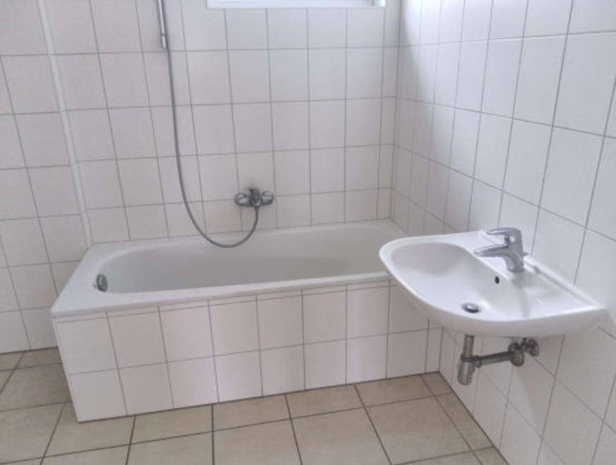 Badezimmer mit weißen Wand- und Bodenfliesen, ausgestattet mit einer Badewanne und einem Waschbecken.