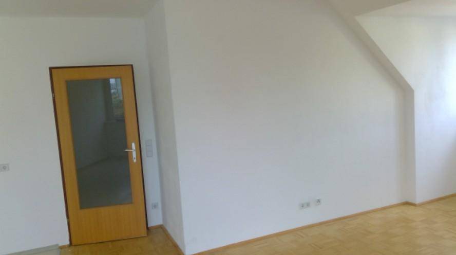 Heller Innenraum mit Holztür, Dachschräge und Parkettboden, bereit zur individuellen Gestaltung.