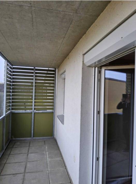 Überdachter Balkon mit Fliesenboden, seitlichen Lamellen und Rollladen am Fenster.