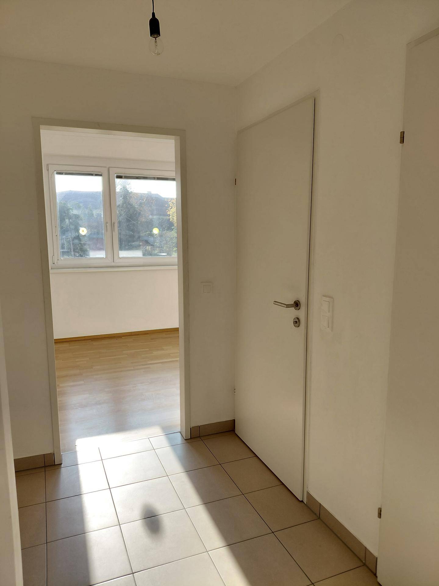 Heller Flur mit Fliesenboden, der zu weiteren Räumen mit Holzboden führt, einladend und funktional.