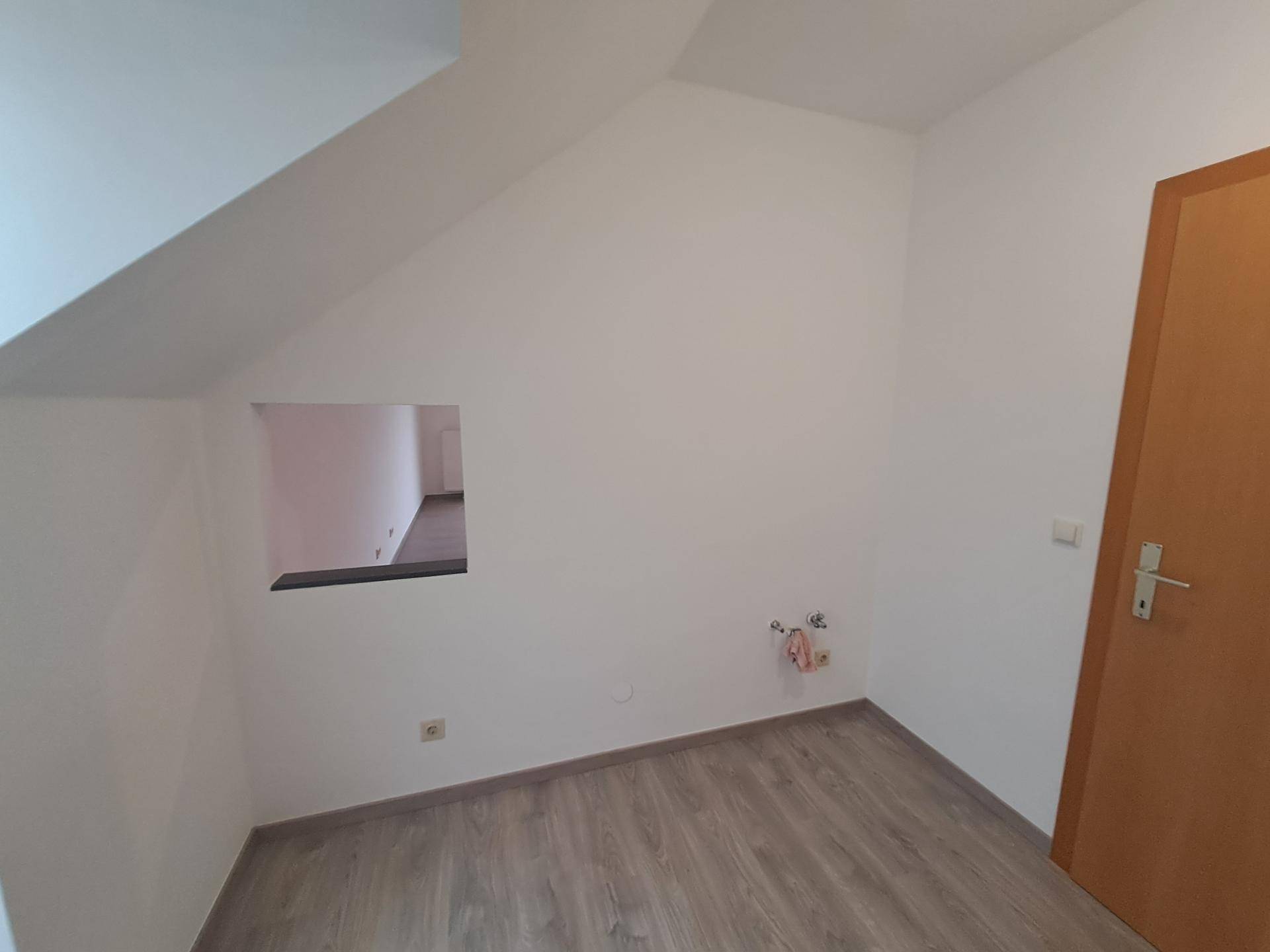 Kleiner Raum mit schräger Decke und Laminatboden, mit einer Öffnung zu einem angrenzenden Bereich.