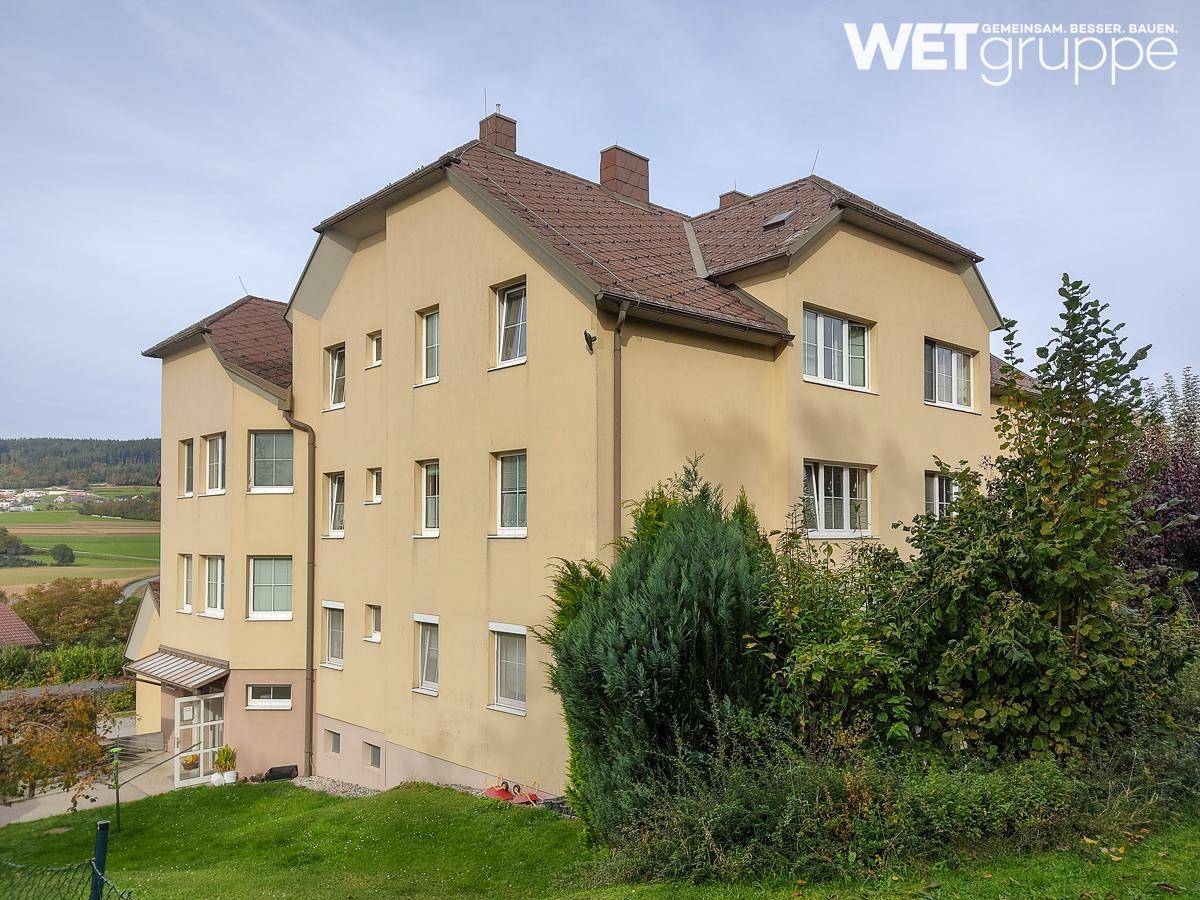 Gesamtansicht des Gebäudes mit gelber Fassade, braunem Dach und weitem Blick in die Landschaft.