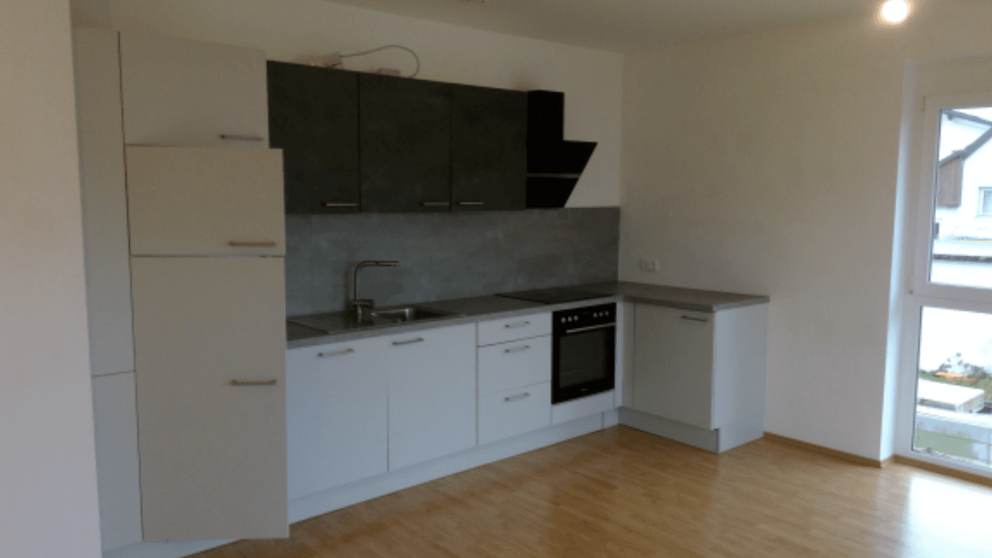 Moderne Einbauküche mit weißen und grauen Schränken, integrierten Geräten und hellem Holzfußboden.